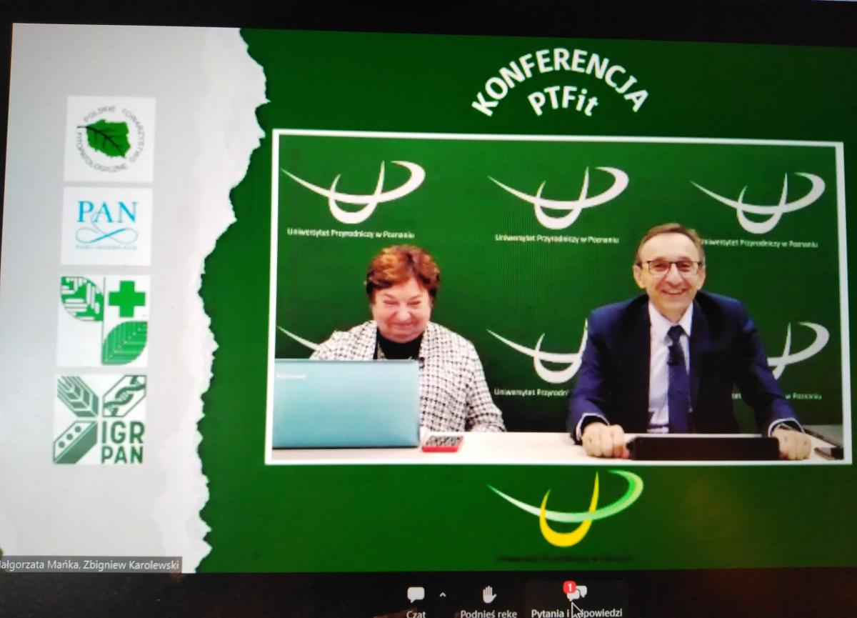 Tło z lewej strony białe a na nim loga PTFiT, PAN, IOR oraz IGR PAN. Pozostała część zielona, na górze białą czcionką napis Konferencja PTFiT, poniżej zdjęcie uśmiechniętych prowadzących konferencję. Kobieta z lewej strony, przed nią laptop. Po prawej mężczyzna w granatowym garniturze.